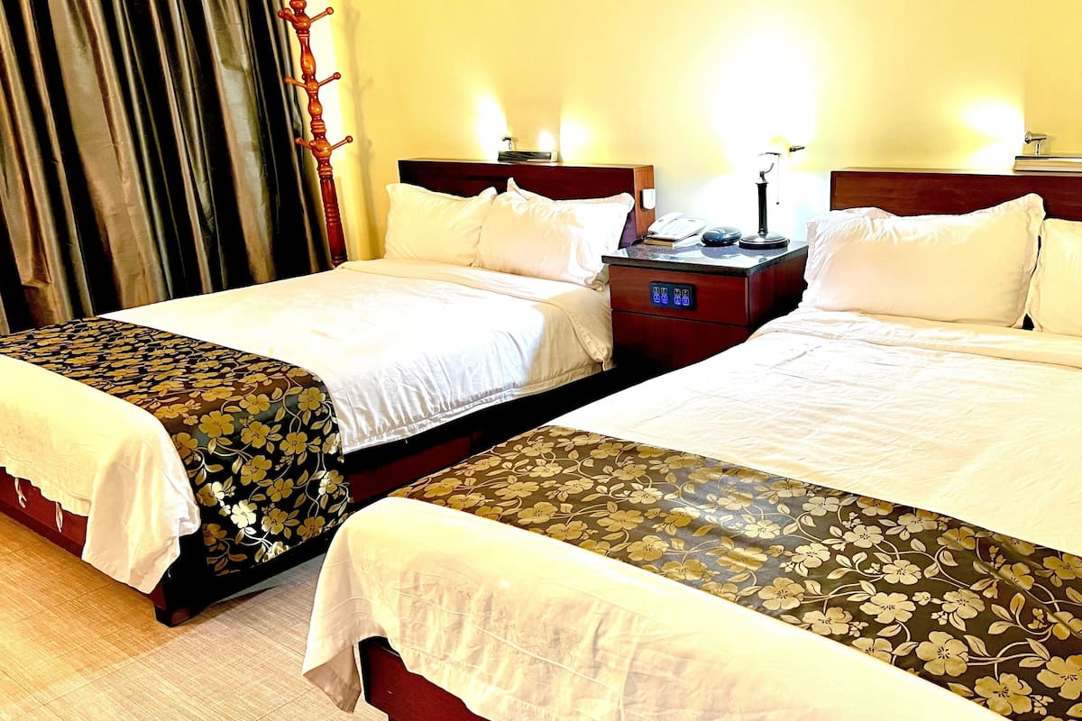 Une chambre d’hôtel avec deux lits, chacun doté d’une tête de lit en bois et de linge de lit blanc. Une table de chevet avec une lampe et un téléphone se trouve entre les deux lits.