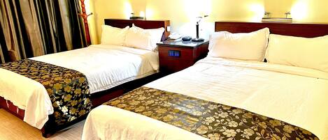 A hotel room with two beds, each with a wooden headboard and white bedding. There is a nightstand with a lamp and a phone between the beds.