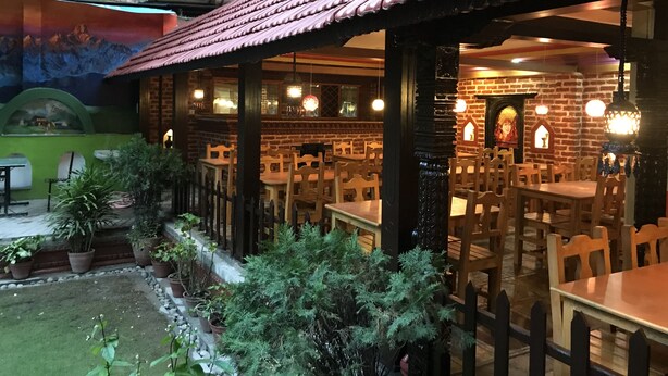 An outdoor dining area with brick walls, wooden tables, and potted plants. - Hotel Green Horizon (Kathmandu)