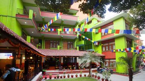 A multi-story building with a green facade, a covered outdoor seating area, and potted plants. - Hotel Green Horizon (Kathmandu)