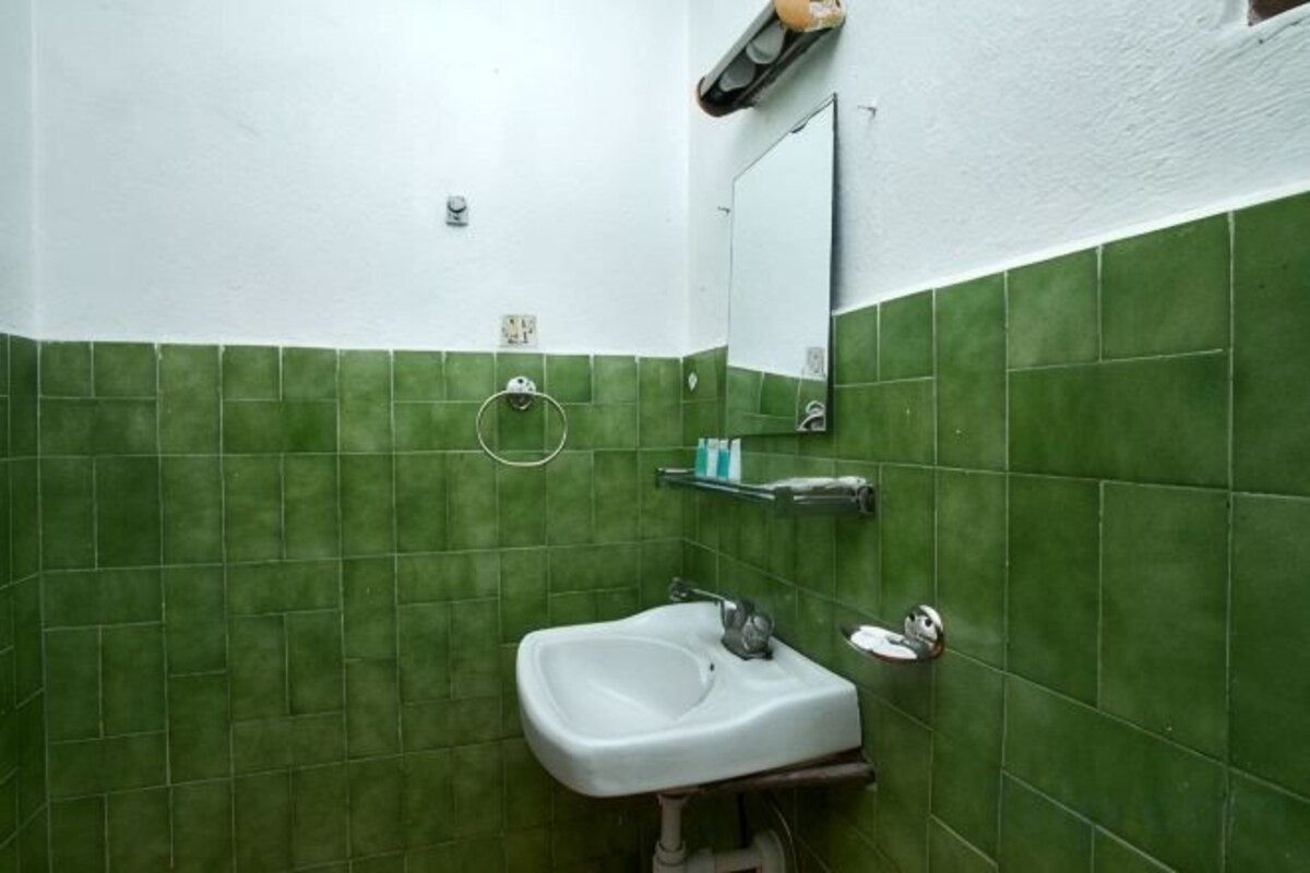A bathroom with green tiles, a white sink, a mirror, and a towel ring.