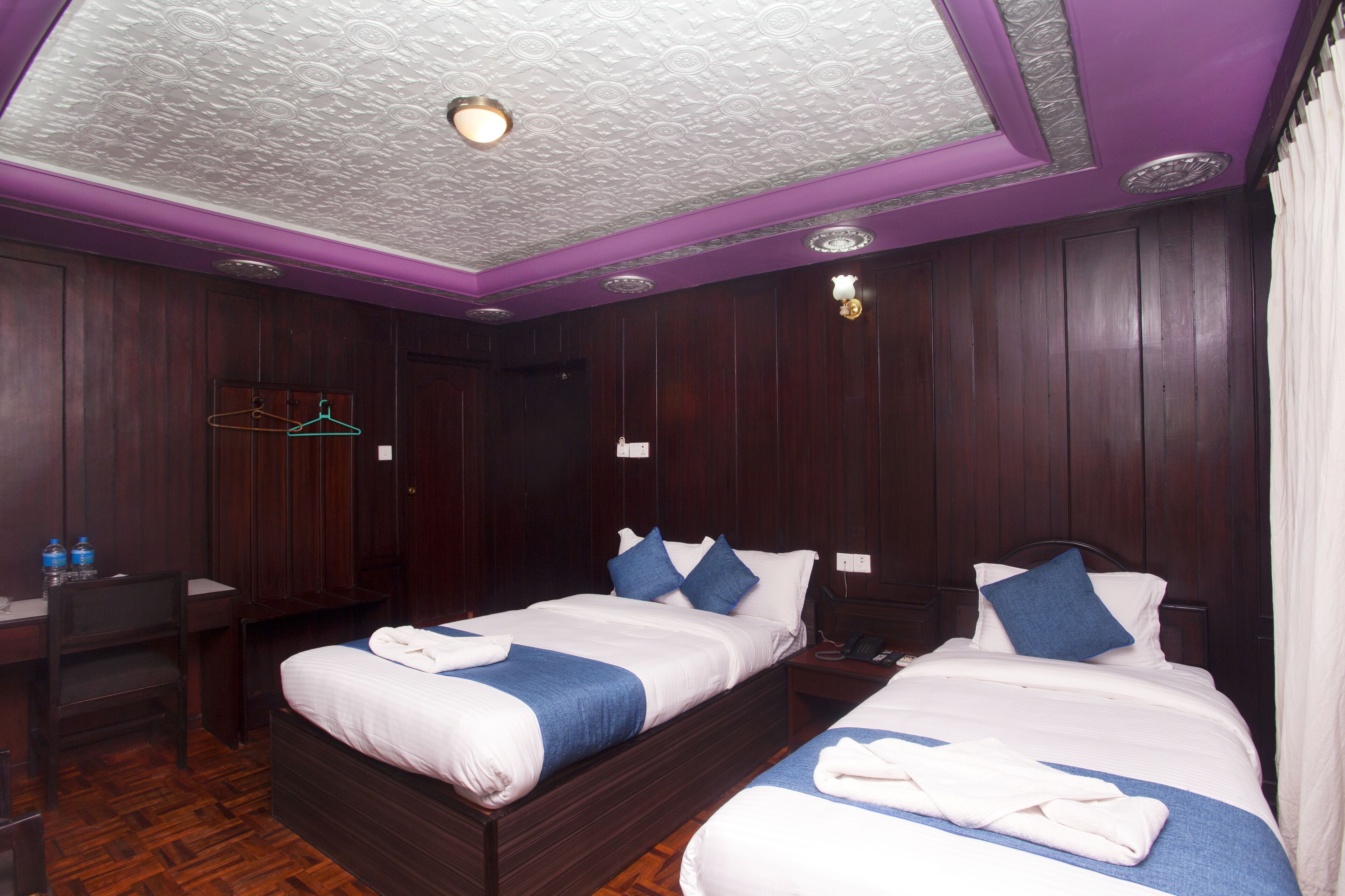 A hotel room with two beds, wooden paneling, and a ceiling with a textured pattern.