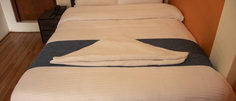 A neatly made bed with a dark headboard, a bedside table with a phone, and a wooden floor.