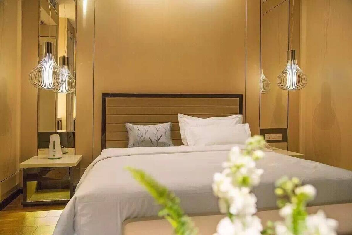 Quarto de hotel com uma cama grande, uma mesinha de cabeceira com abajur e um espelho na parede.