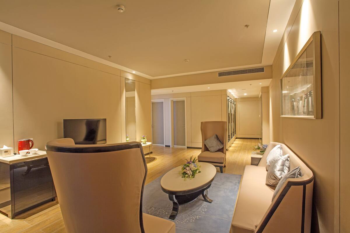Quarto de hotel moderno com sofá, poltrona e uma pequena mesa com um vaso de flores.