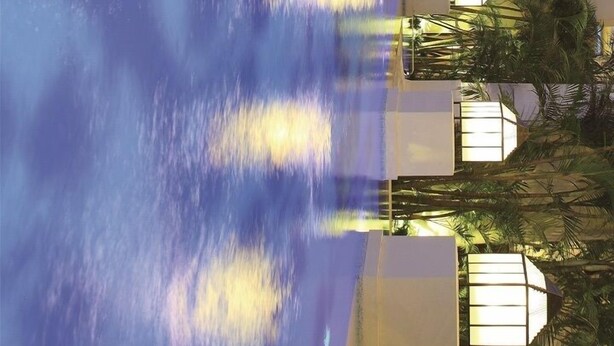 Een hotel met een zwembadgedeelte, inclusief waterstralen, palmbomen en een gebouw met een lichtgekleurde gevel.