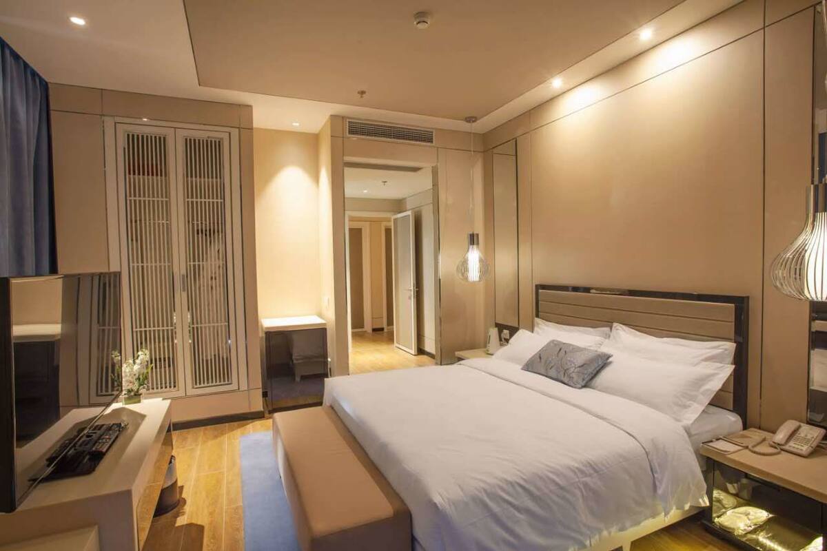 Quarto de hotel moderno com uma cama grande, mesas de cabeceira, escrivaninha e um guarda-roupa.
