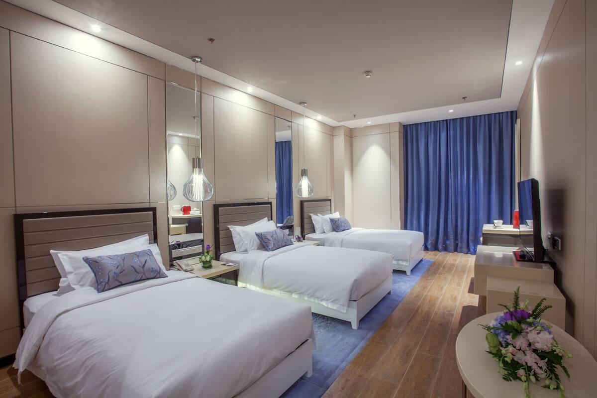 Quarto de hotel com duas camas, uma escrivaninha, um espelho e uma televisão.