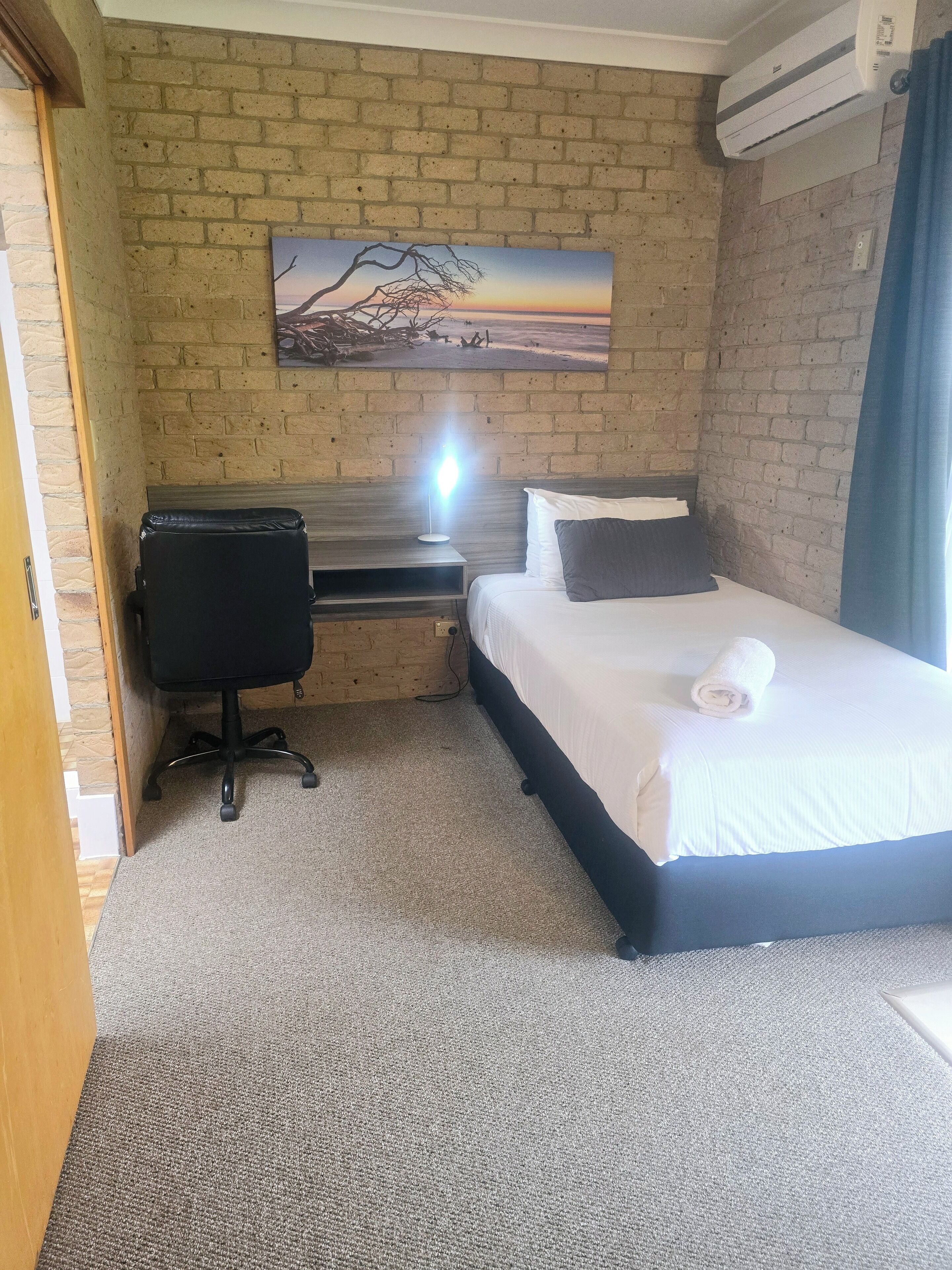 A hotel room with a bed, a desk, a chair, and a painting on the wall.