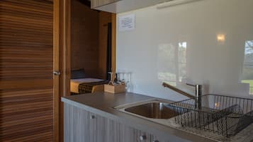A modern kitchen with a wooden door, a sink with a black dish rack, and a small countertop with a candle holder and glassware.