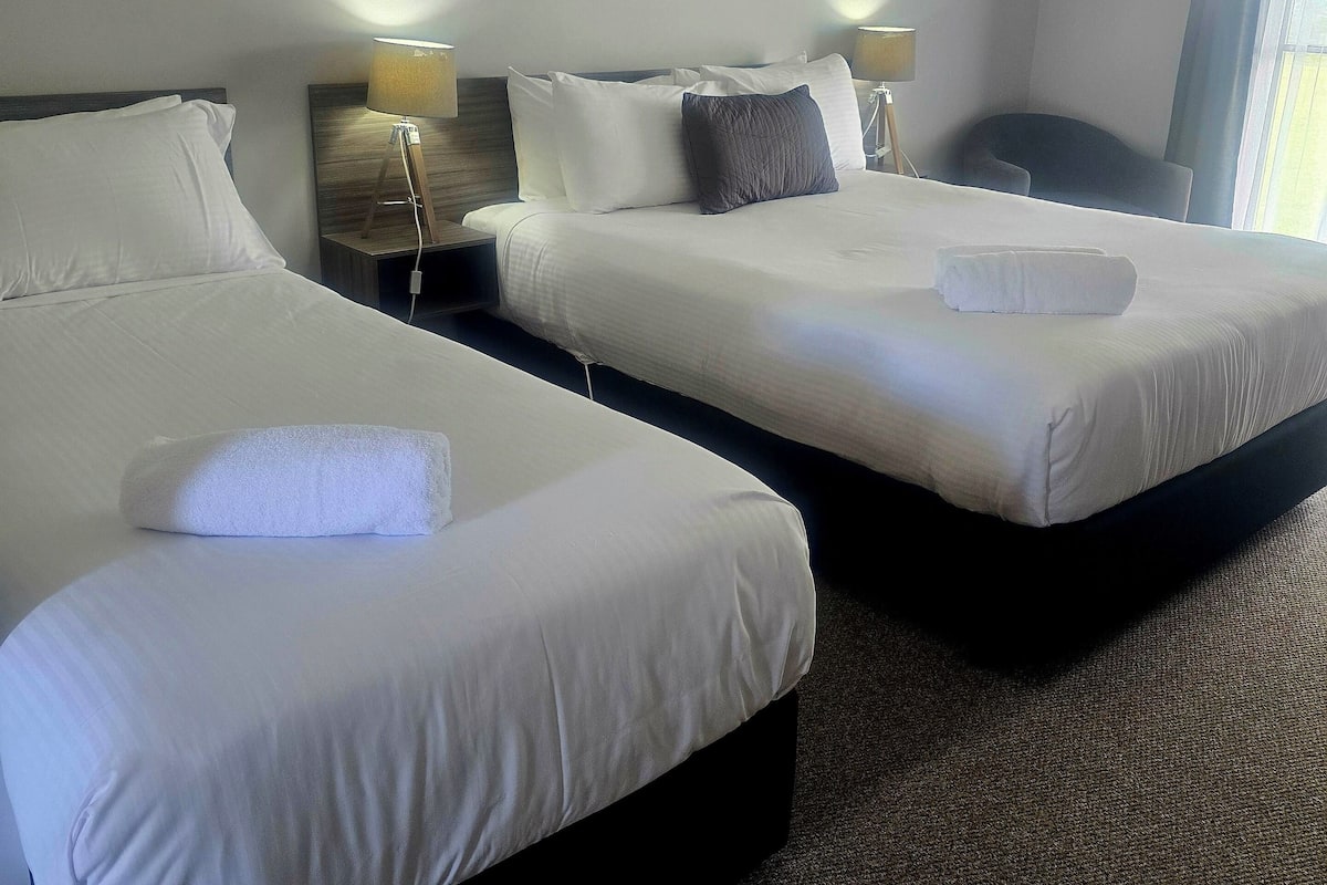 A hotel room with two beds, a painting on the wall, and an air conditioning unit.