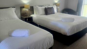 A hotel room with two beds, a painting on the wall, and an air conditioning unit.