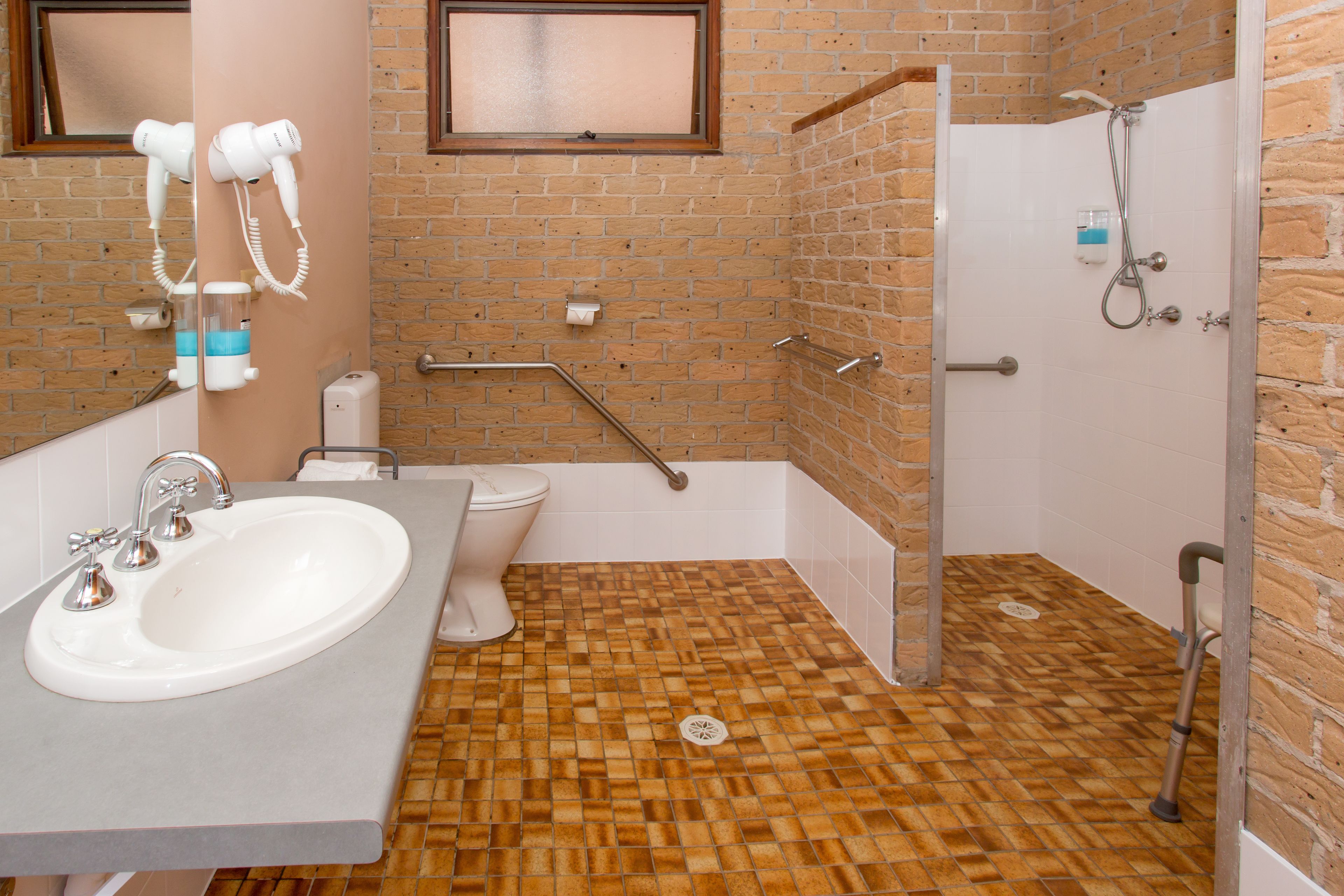 Un baño con lavamanos, inodoro y zona de ducha con barra de apoyo.