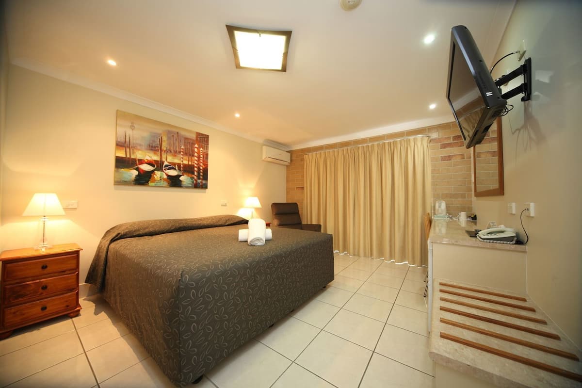 A hotel room with a bed, a desk, a chair, a TV mounted on the wall, and a bathroom with a shower curtain.