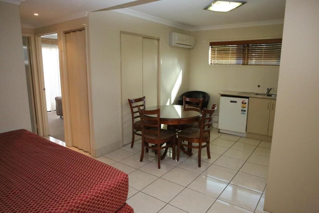 A compact hotel room with a bed, a dining table with chairs, a kitchenette, and a bathroom door.