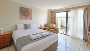 Une chambre d’hôtel avec un grand lit, une chaise, un tableau et une vue sur l’extérieur, accessible par une porte coulissante.