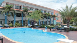 Une piscine entourée de chaises longues et de palmiers, avec un immeuble à plusieurs étages en arrière-plan.