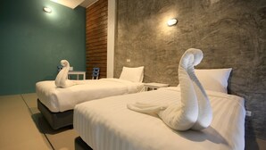 Deux lits avec du linge de lit et des serviettes blanches disposés en forme de cygne, une petite table et un mur au revêtement texturé.