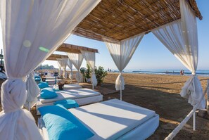 A beachside lounge area with white canopies and blue cushions, overlooking the beach. - Helios Hotel - All Inclusive (Manavgat)