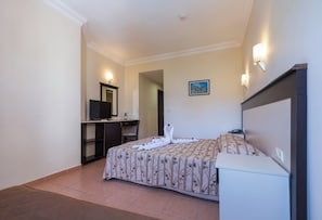 A hotel room with a bed, a desk with a television, a mirror, and a painting on the wall.