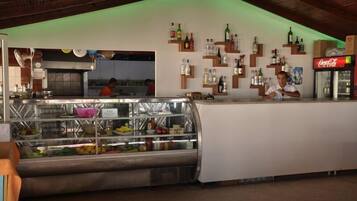 Una zona de bar con una vitrina llena de frutas y un refrigerador de Coca-Cola.