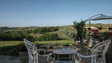 Una terrazza con sedie e tavolo in ferro battuto bianco, con vista su un vigneto e case in lontananza.