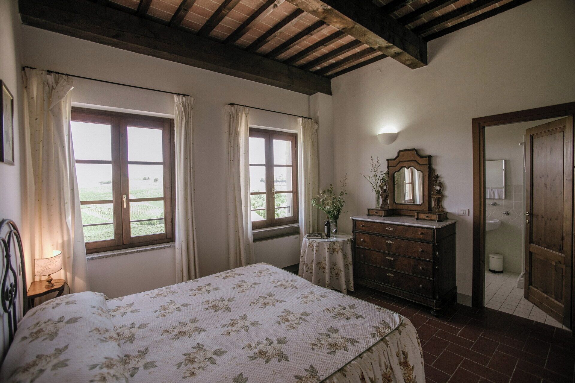 Une chambre à coucher comprenant un lit, une commode, un miroir et deux fenêtres avec des rideaux.