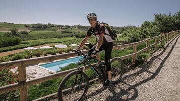 A person on a mountain bike near a pool with a wooden fence and greenery in the background.