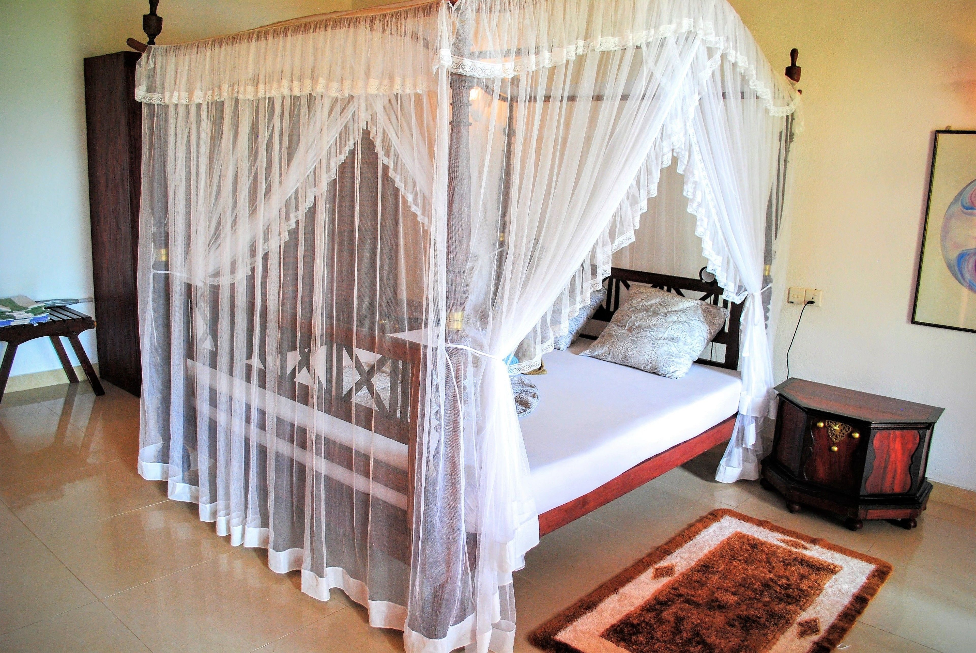 A bedroom with a four-poster canopy bed, a bedside table, and a nightstand.