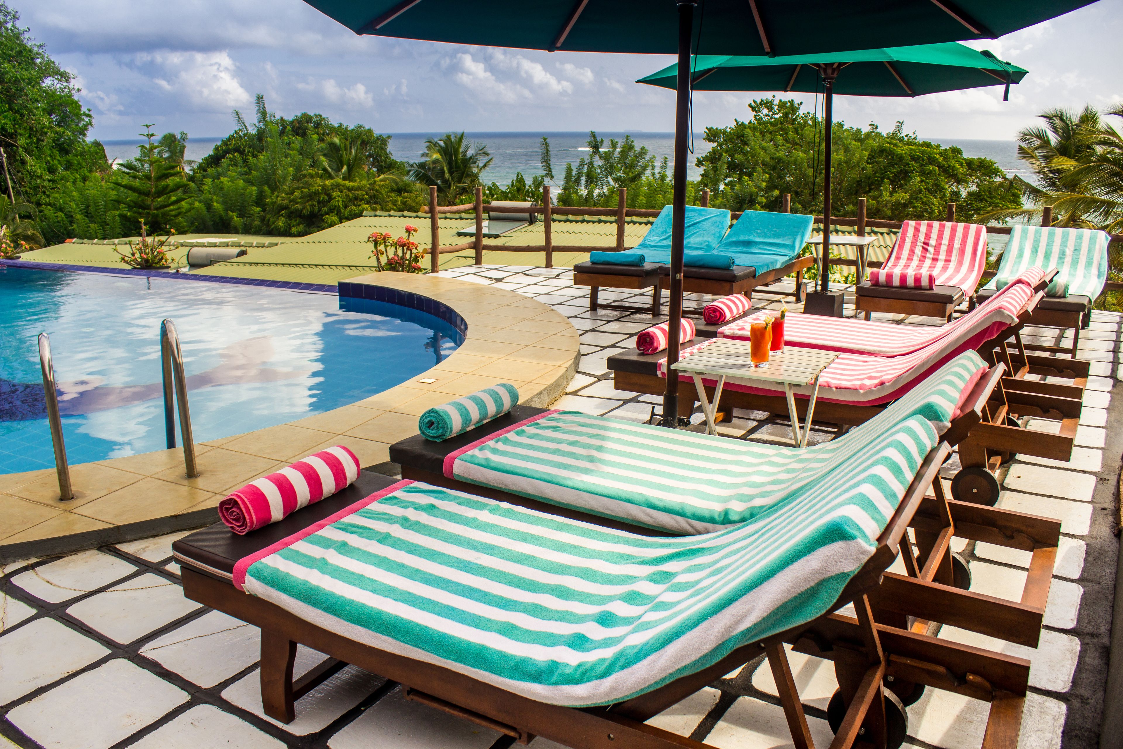 A poolside area with lounge chairs and umbrellas, a pool, and a view of the ocean.