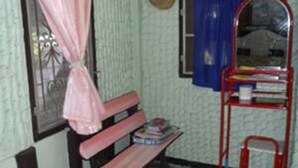 A small, cozy room with a patterned floor, a bench, a red chair, a window with a curtain, and a shelf with books. - View Point Lodge (Mae Hong Son)