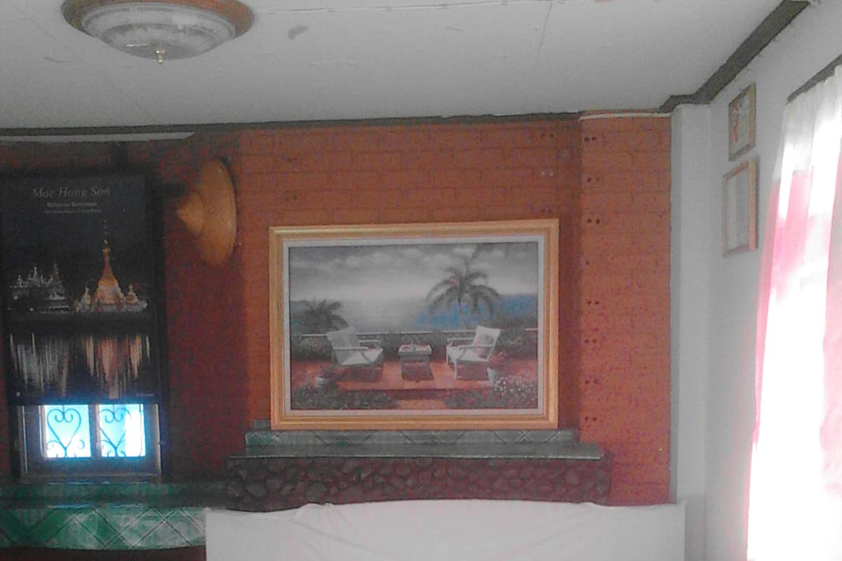Una habitación de hotel con cama, un cuadro de una playa, una ventana con vistas a palmeras y una mesita con una lámpara.