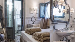 A bedroom with a bed, a bedside table, a mirror, a window with curtains, and a bathroom with a sink and mirror. - Il Giardino d'Ulisse (Reggio Calabria)