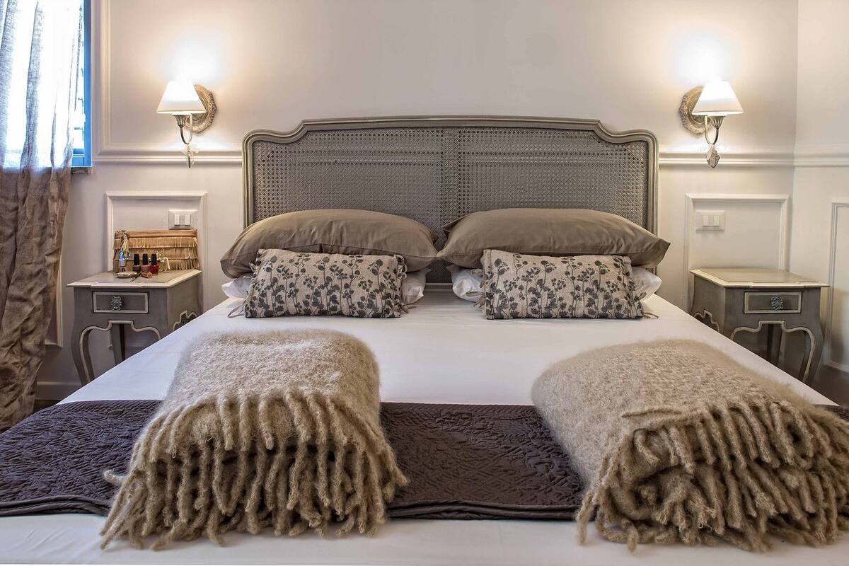Un lit bien fait, doté d’une tête de lit en rotin, de deux tables de chevet avec des lampes et d’un coussin à motifs floraux.