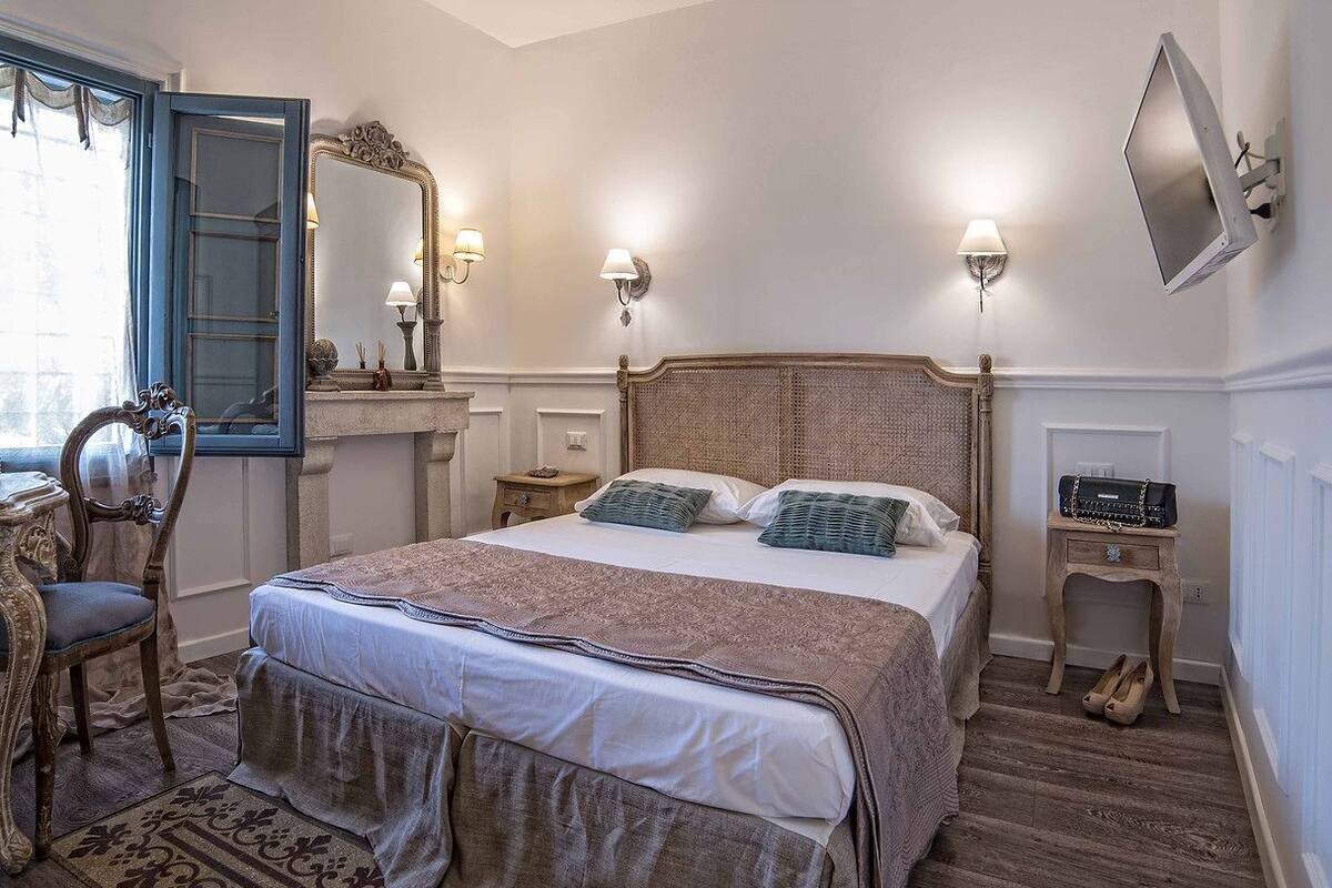Une chambre à coucher avec un grand lit, une chaise, une commode, un miroir et un téléviseur fixé au mur.
