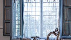 A room with a table and a chair, a window with curtains, and a patterned rug. - Il Giardino d'Ulisse (Reggio Calabria)