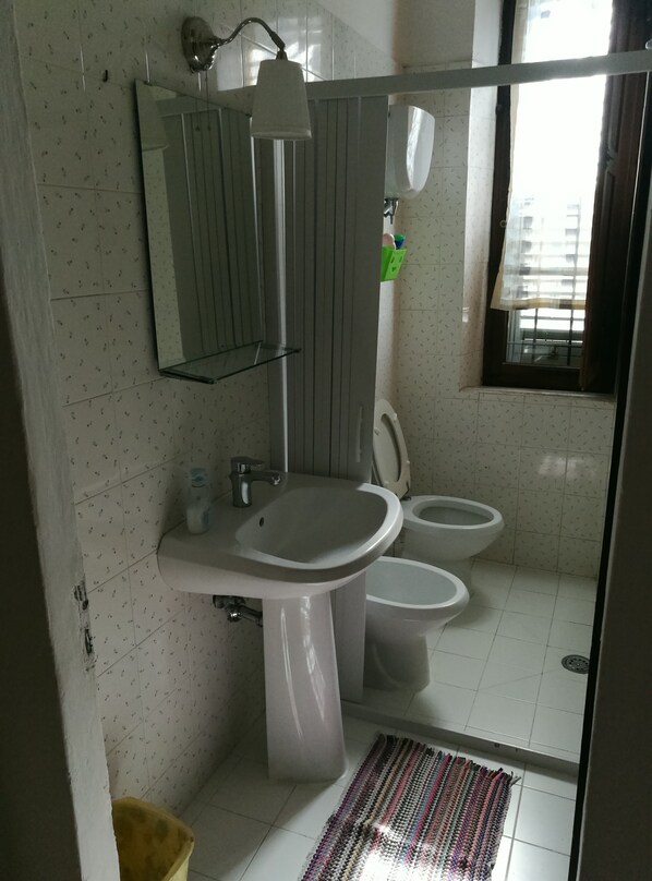 A bathroom with a sink, two toilets, a mirror, and a window.
