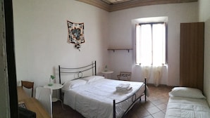 A bedroom with a bed, a small table, a chair, a window with curtains, and a decorative wall hanging. - Casa di Alfredo (Siena)