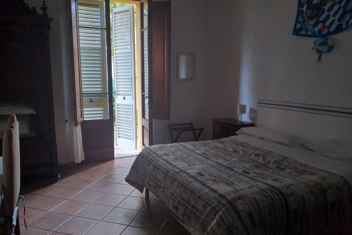 A bedroom with a bed, a chair, a nightstand, a lamp, and a door with shutters.