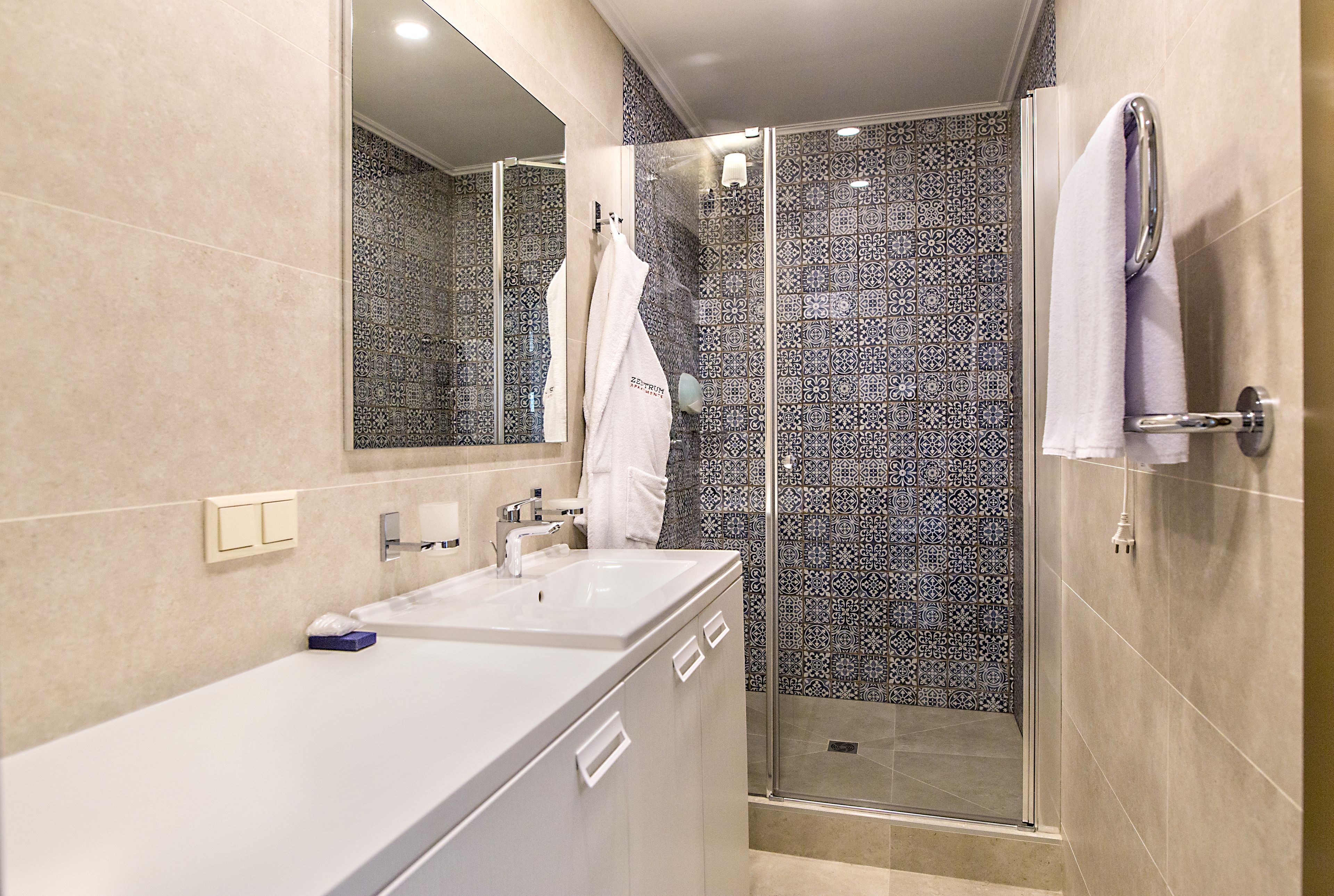 Un bagno moderno con un ampio specchio, due lavabi, una doccia con porta in vetro e piastrelle decorate.