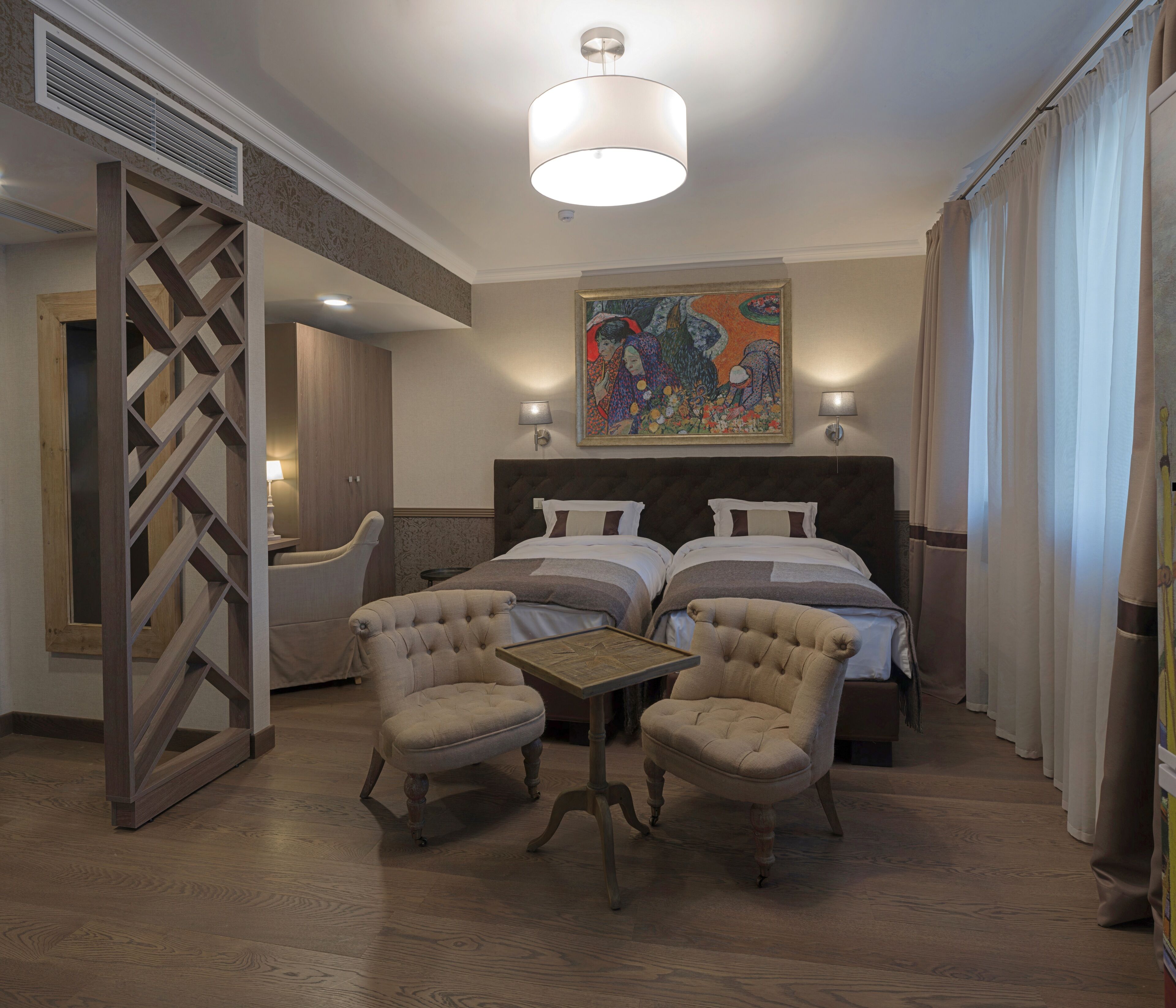 A hotel room with a bed, two armchairs, a small table, a painting, and a window with curtains.