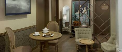 A hotel room with a round wooden table, two chairs, a sofa, a mirror, and a decorative partition.