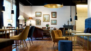 Un salon moderne avec un plancher en bois, un canapé bleu, un fauteuil marron et un pouf bleu. Des tableaux encadrés ornent le mur, ainsi qu’une cheminée et une lampe posée sur une table d’appoint.