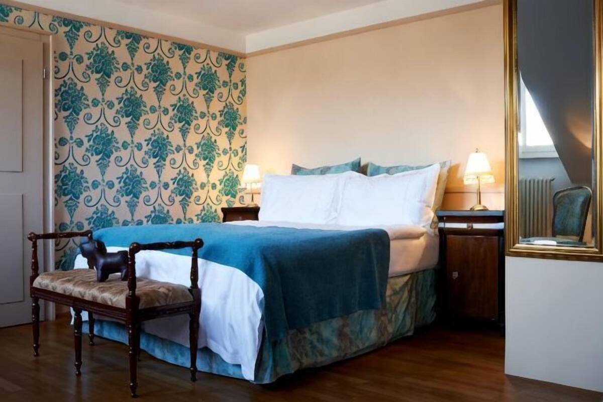 Ein Schlafzimmer mit Bett, Sessel, Nachttisch, Lampe und Spiegel.