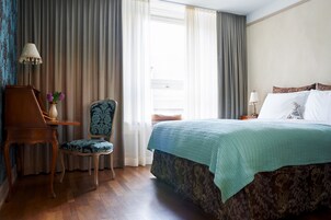 Hotellihuone, jossa on sänky, tuoli, työpöytä ja lamppu.