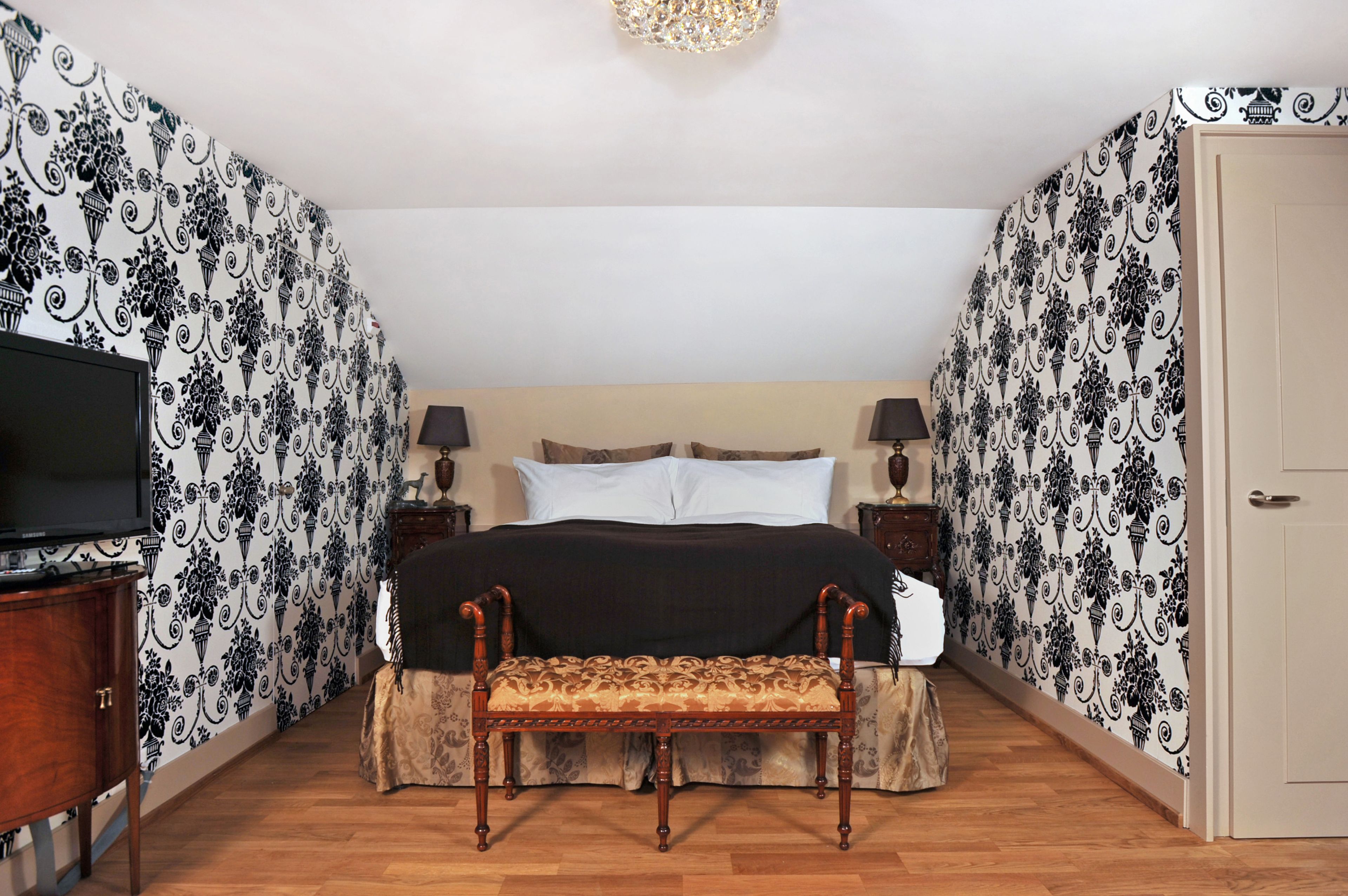 A bedroom with a bed, bedside tables, a bench, and a television.