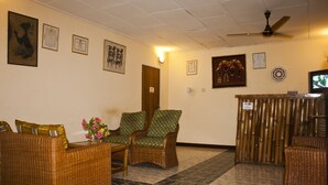 A lobby with wicker furniture, a reception desk, and framed certificates on the wall. - Joy Family Lodge (Amasaman)