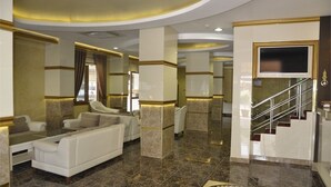 A spacious lobby with a marble floor, a sofa set, a television mounted on the wall, and a staircase. - Ugur Hotel (Mersin)