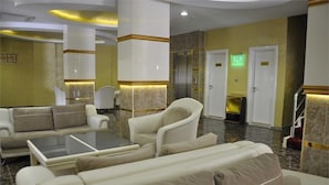 A hotel lobby with a seating area, a glass-top table, and a reception desk. - Ugur Hotel (Mersin)