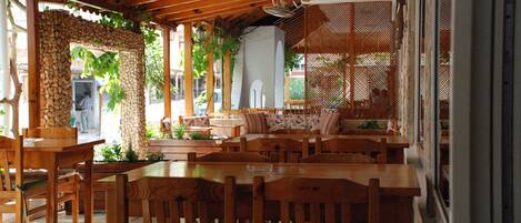 An indoor dining area with wooden tables and chairs, stone walls, and a view of the street outside.